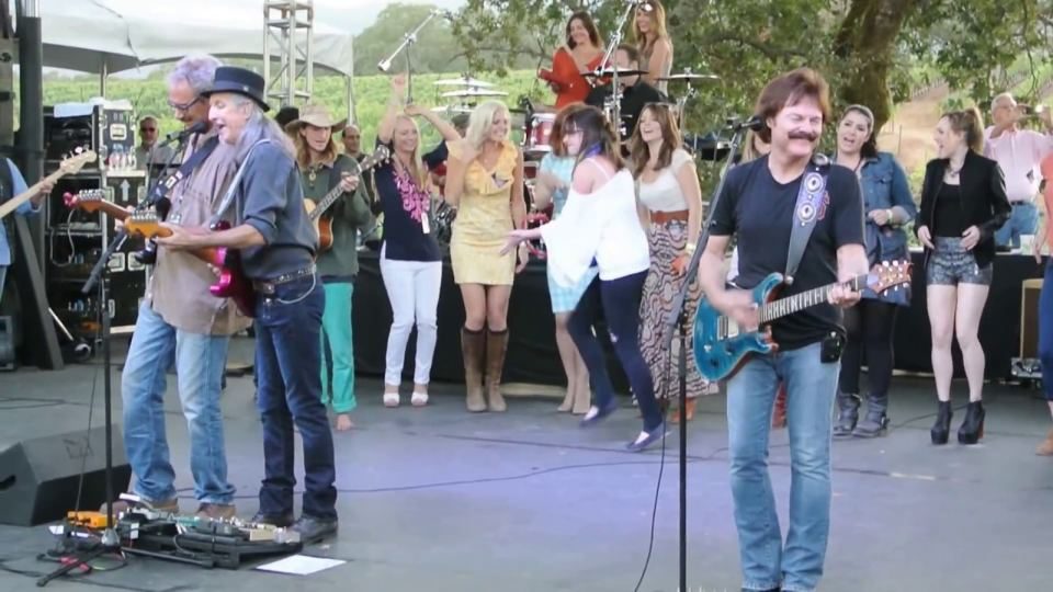 The Doobie Brothers on stage, guitars up, crowd dancing behind them.